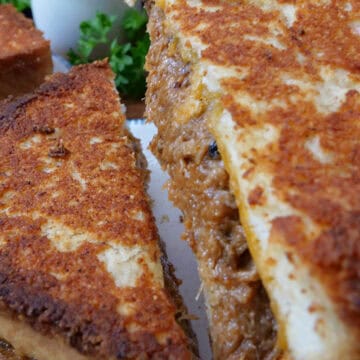 A close up of a pulled pork grilled cheese sandwich but in half and one of the halves being lifted off the plate.