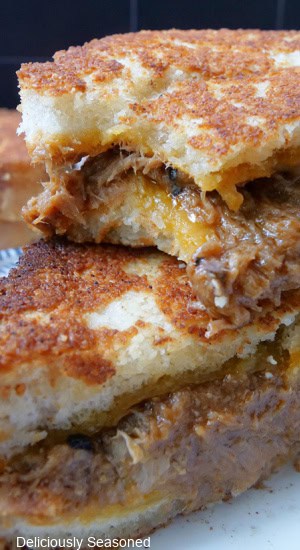 Two halves of pulled pork grilled cheese stacked on top of each other with a bite taken out of the one on top.
