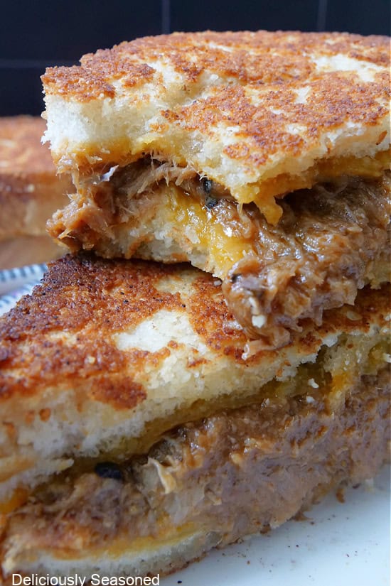 A close up of two pulled pork grilled cheese halves with a bite taken out of one of the halves.