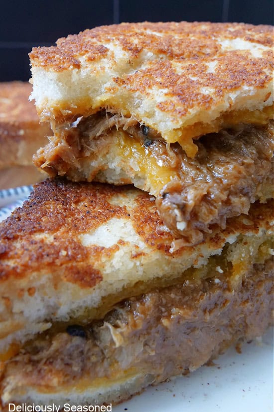 Two pulled pork grilled cheese halves stacked on top with a bite taken out of one.