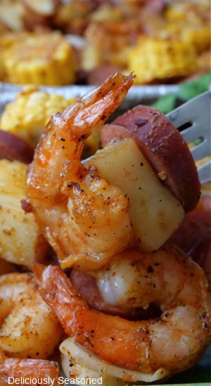 a close up of a bite of shrimp, potato and smoked sausage on a fork.