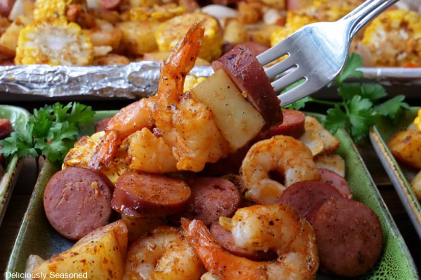 A horizontal photo of a green plate filled with a serving of shrimp, sausage, potatoes, and corn.