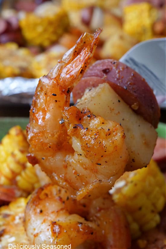 A close up photo of shrimp, potato, and smoked sausage on a fork.
