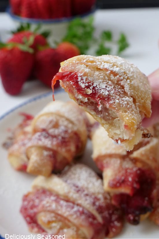 A close up of a mini pastry filled with strawberry and cream cheese that has a little bite taken out of it.