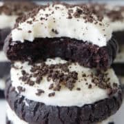 Two brownie cookies with white frosting on them with one of the cookies has a bite taken out of it.