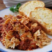 A white plate with a serving of pasta with two pieces of cheese bread on the plate.