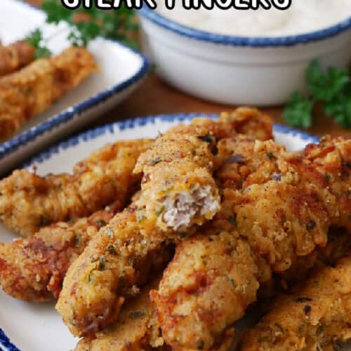 A white plate with blue trim with crispy country fried steak fingers on it.