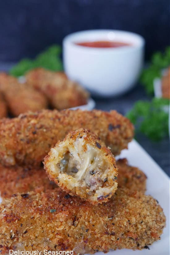 A white plate with a few spicy mozzarella sticks on it with one cut in half showing the inside ingredients.