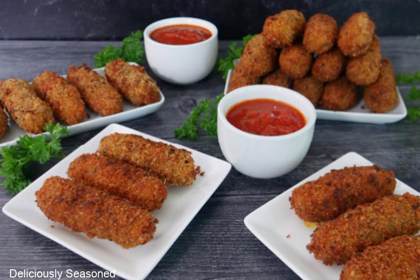A grey wood surface with spicy mozzarella sticks on white plates with two small white bowls filled with marinara sauce.