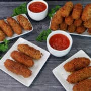 A gray wood surface with white plates filled with fried mozzarella sticks on them.