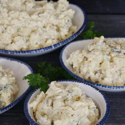 Four white bowls with blue trim with potato salad in each one of the bowls.