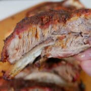A smoked pork rib held above a rack of ribs.
