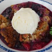 A white bowl with blue trim with strawberry blueberry cobbler in it.