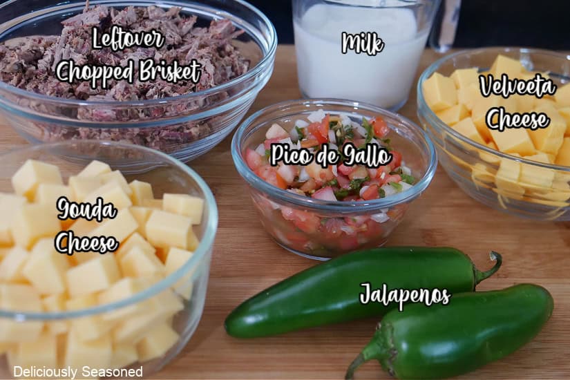 A wood surface with the six ingredients, that are labeled, that it takes to make leftover brisket queso.