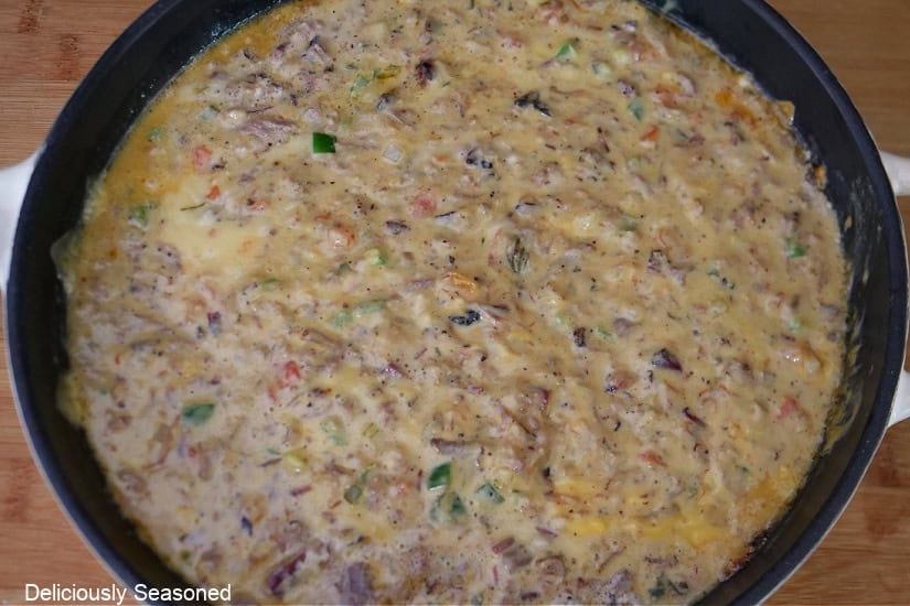 A wood surface with a white cast iron pan filled with smoked brisket queso.