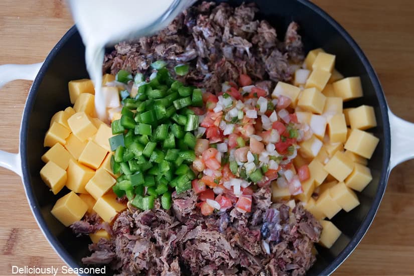 A white cast iron pan with the six ingredients needed to make leftover smoked brisket queso.