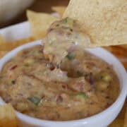 A white bowl filled with brisket queso and a chip that has been dipped in the queso.