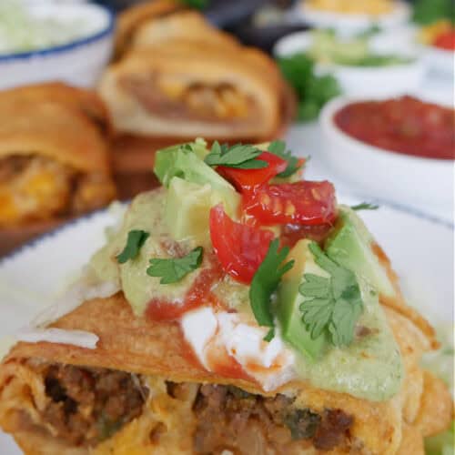 A piece of taco crescent ring on a white plate sitting on shredded lettuce with different toppings on top.