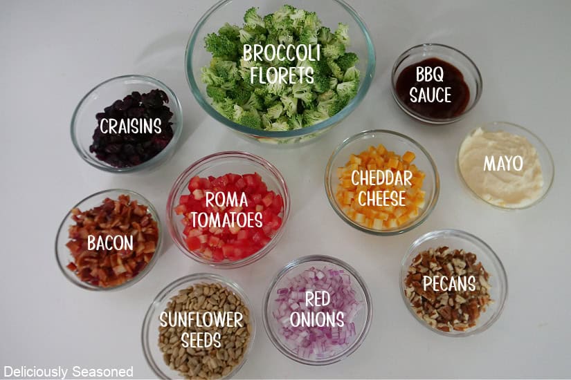 A white surface with glass bowls filled with all the ingredients needed to make broccoli salad.