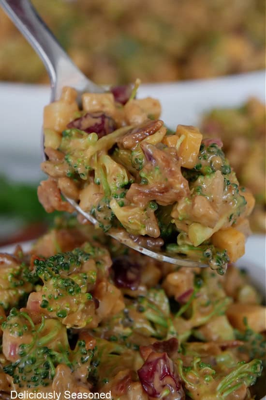 A spoonful of broccoli salad held above a bowl filled with the broccoli salad.