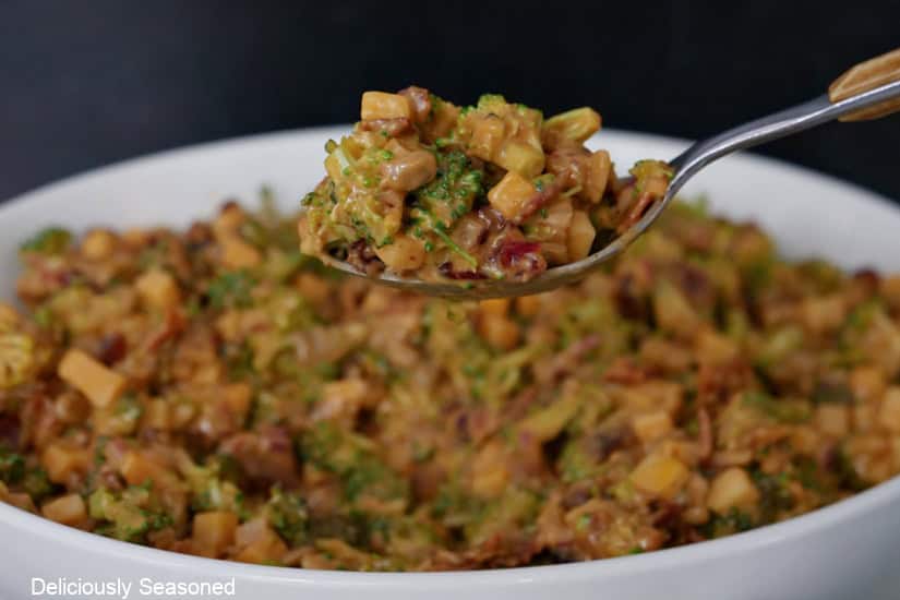A large white bowl with broccoli salad in it and a serving spoon scooping out a spoonful.