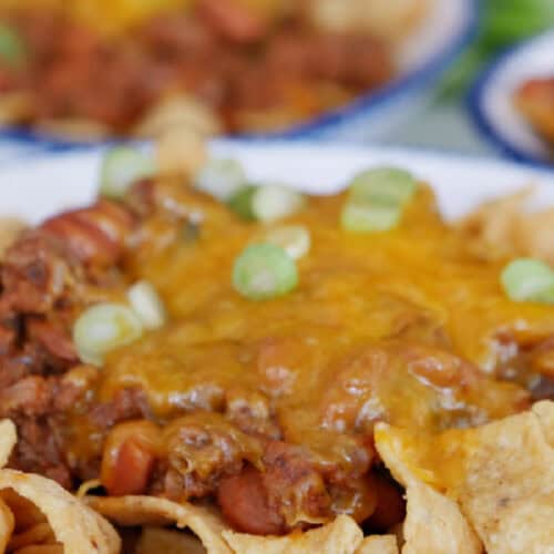 A white bowl with blue trim with chili cheese Fritos in it.