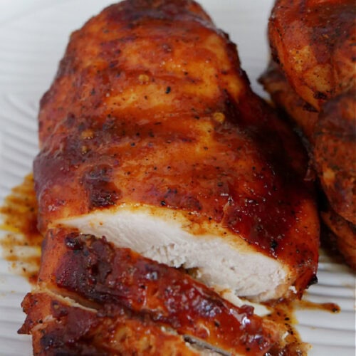 A white plate with a smoked chicken breasts on it.