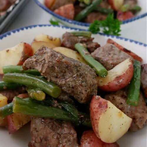A white bowl with blue trim with a serving of steak potatoes and green beans in it.