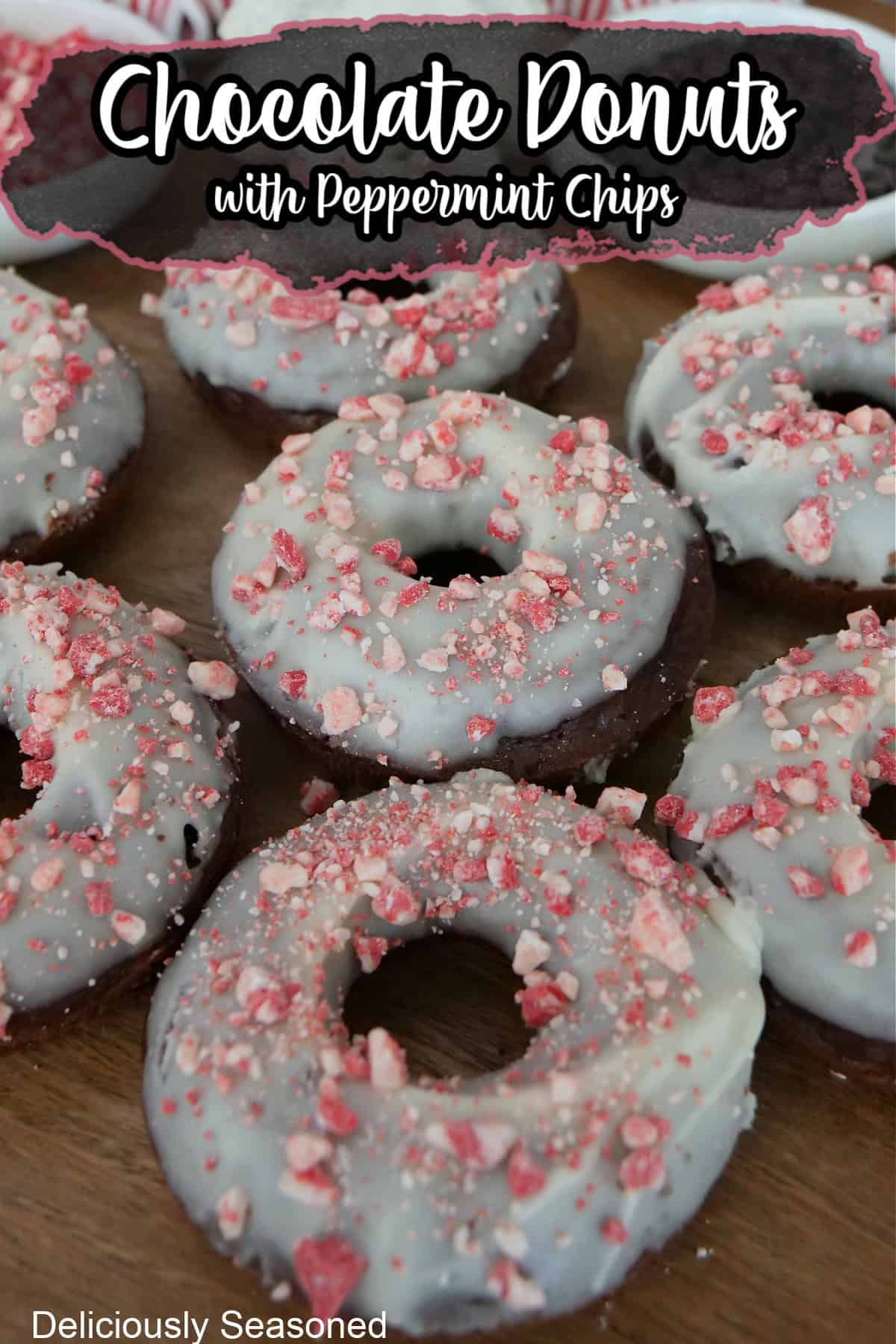 A wood surface with homemade chocolate donuts with white icing and peppermint chips on top.