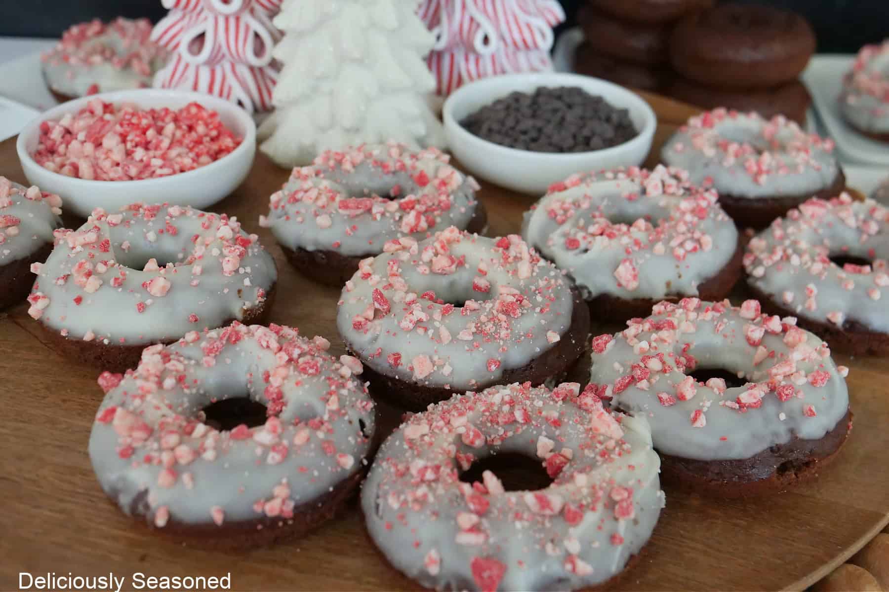 A wood surface with iced chocolate donuts on it with holiday decorations in the background.
