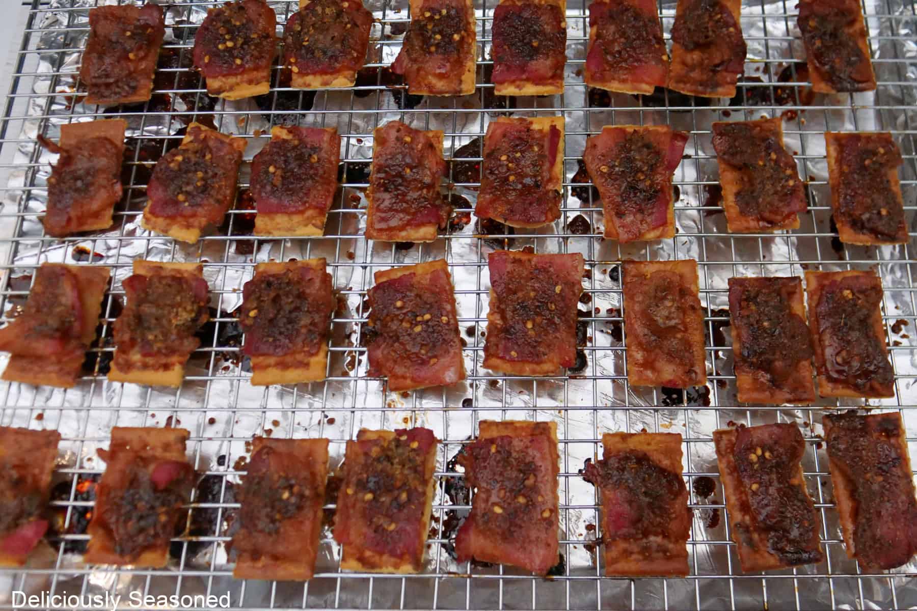 A wire rack on a foil lined baking sheet with candied bacon crackers on it.