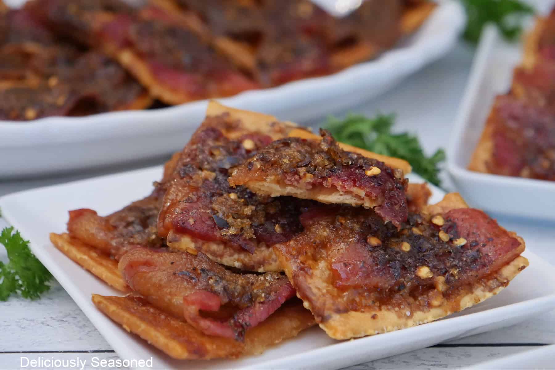 A white surface with candied bacon crackers on a white plate.
