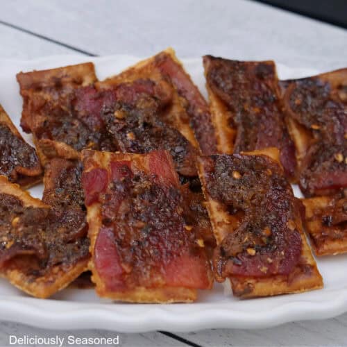 A white plate with candied bacon crackers on it.
