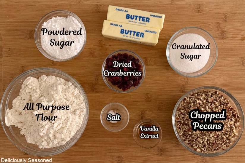 A wood surface with all the ingredients needed to make cranberry pecan snowball cookies.