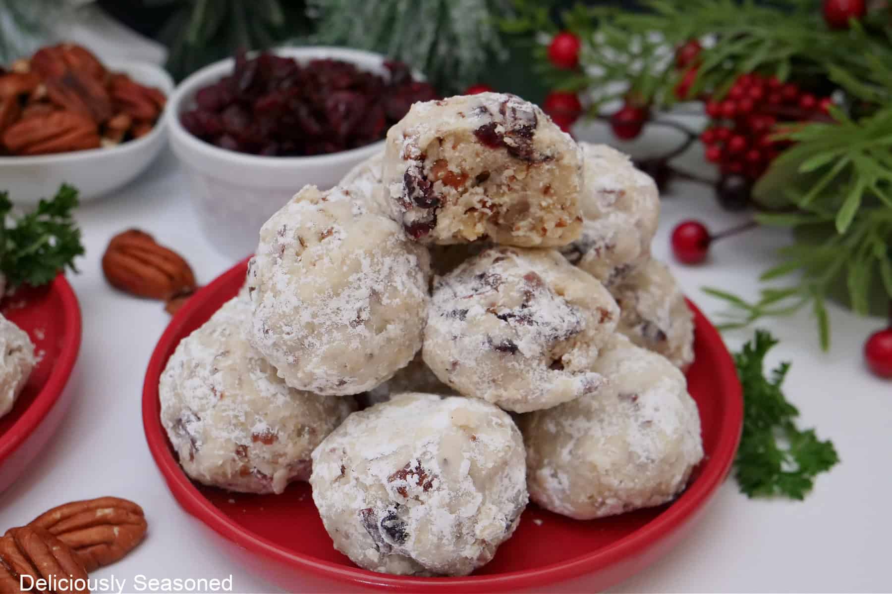 A white surface with a red plate with snowball cookies stacked up on each other.