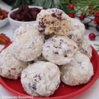 A red small round plate with a stack of 10 snowball cookies on it.