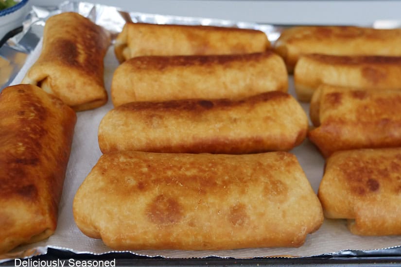 A baking sheet lined with parchment paper with fried burritos on it.