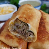 A few fried burritos on a plate stacked on top of each other with a few bites out of the top one.
