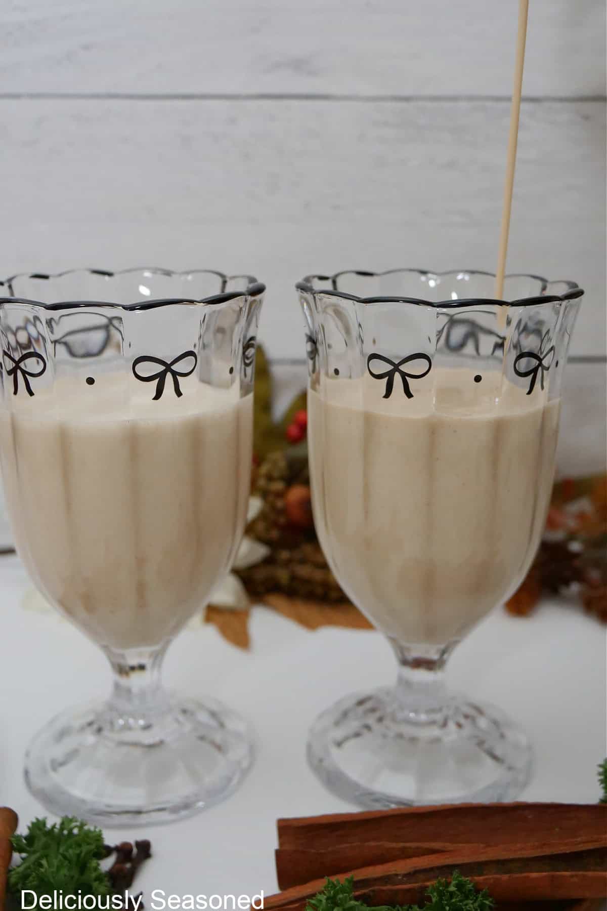 Two glasses filled with eggnog on a white surface.