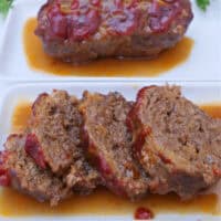A white surface with two mini meatloaves on it and one is sliced into bite-size pieces.