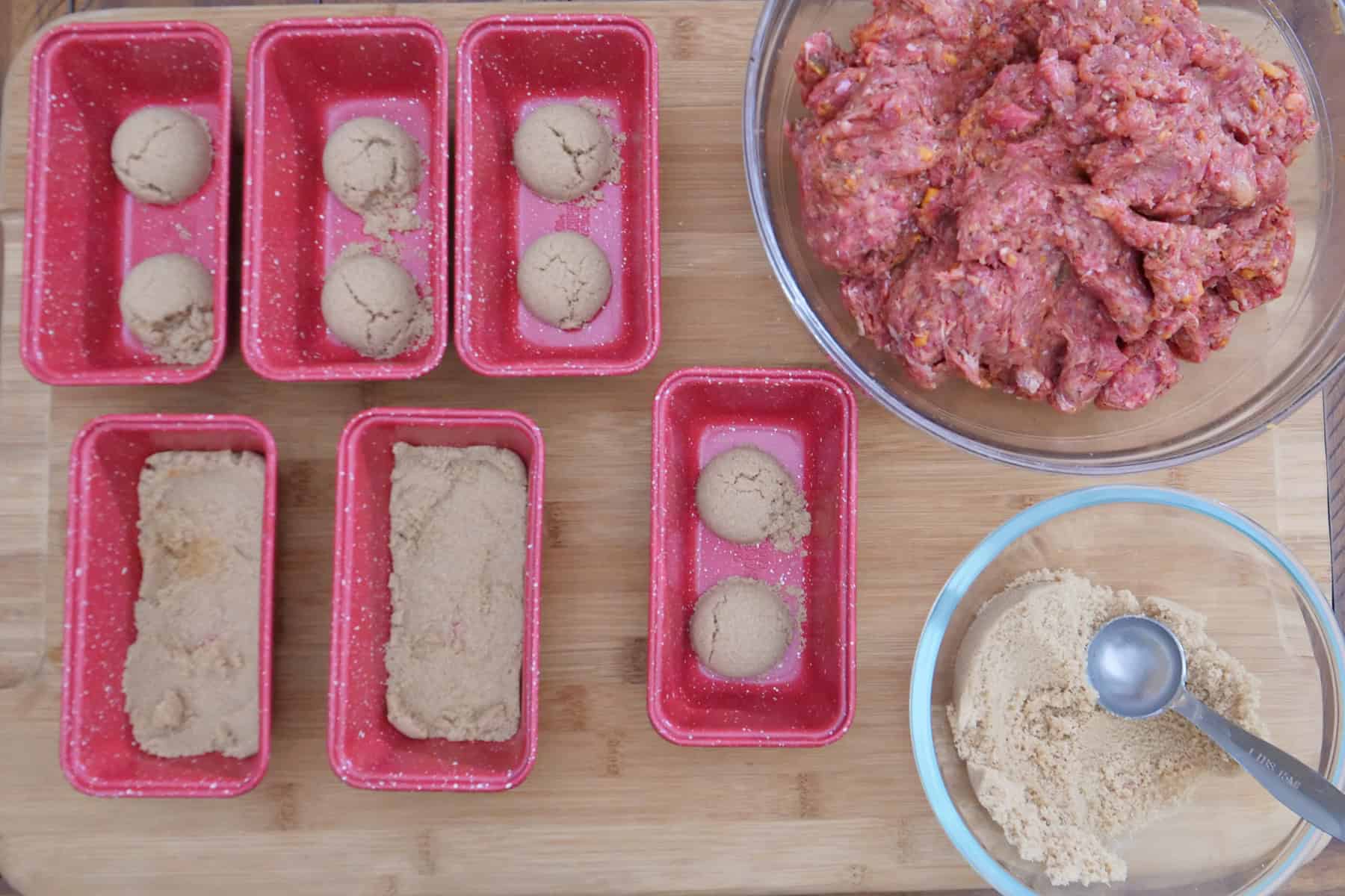A wood surface with red mini loaf pans with brown sugar in them.