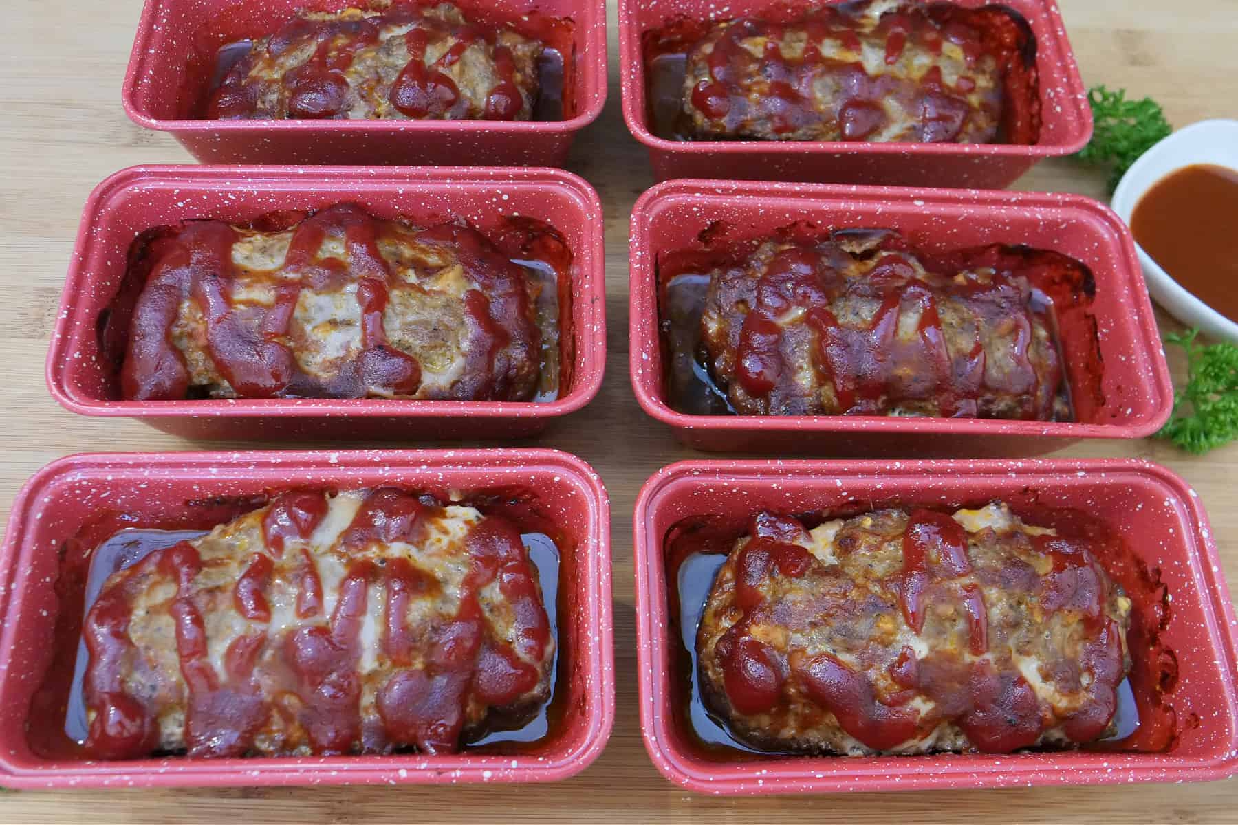 Six mini red loaf pans with baked meatloaves in them.