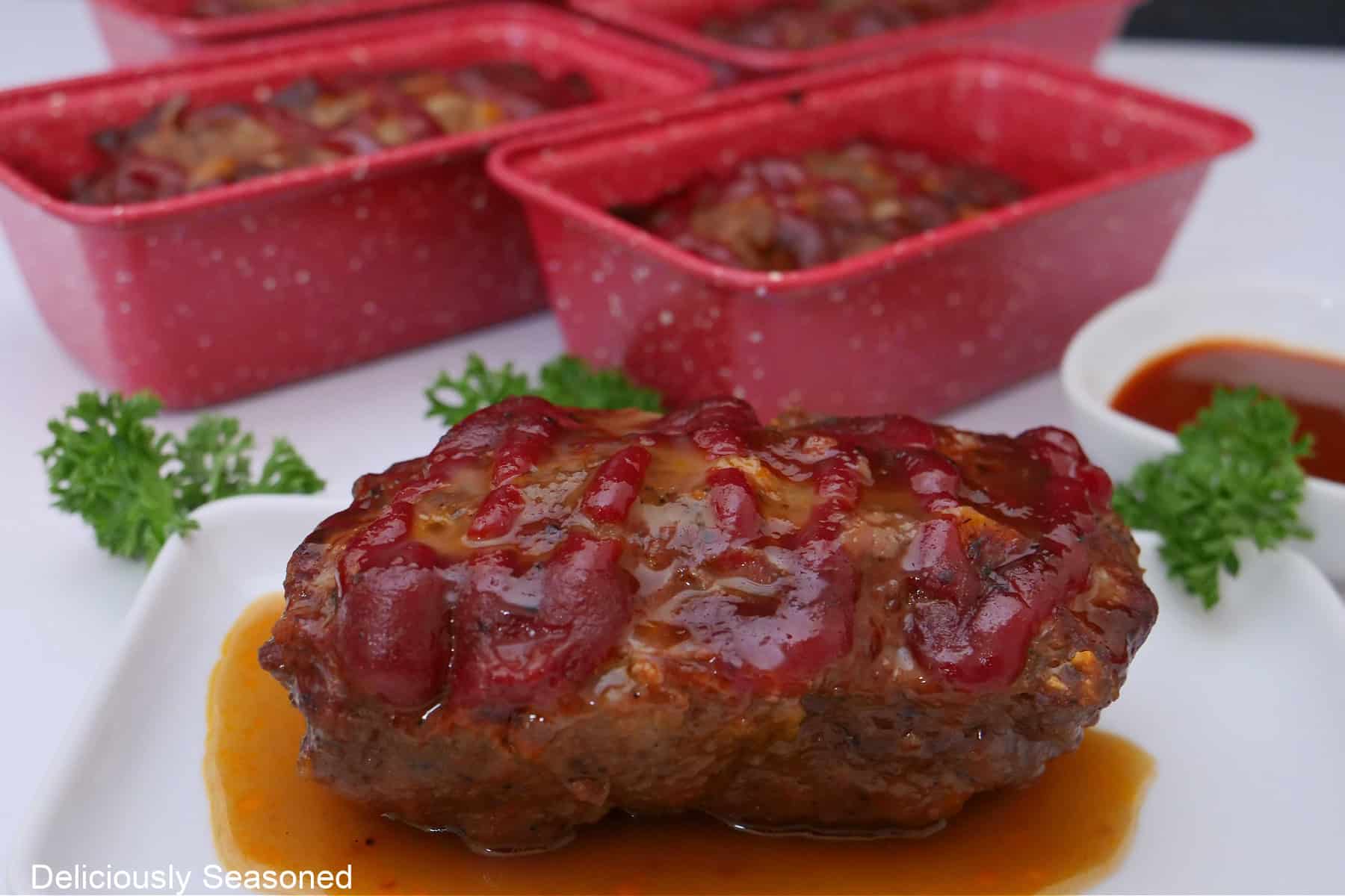 A white plate with a mini brown sugar meatloaf on it with more in the background.