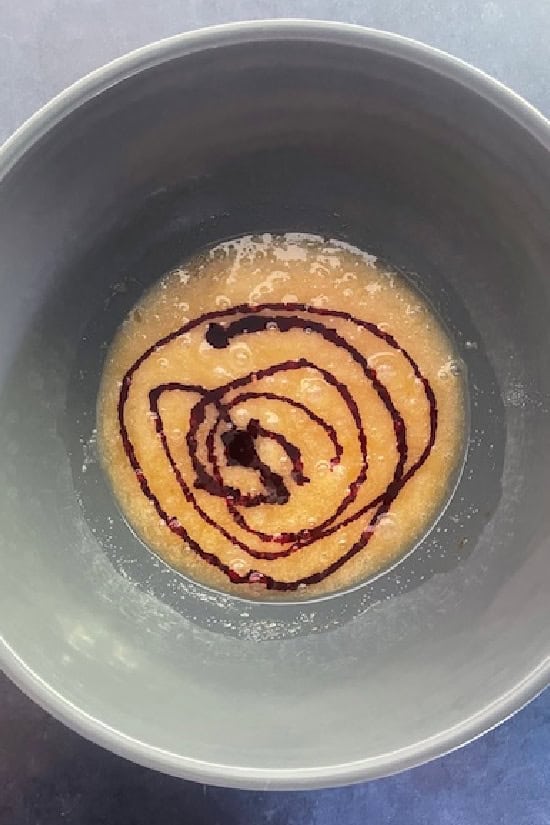 A grey bowl with the wet ingredients and red gel food coloring in it.