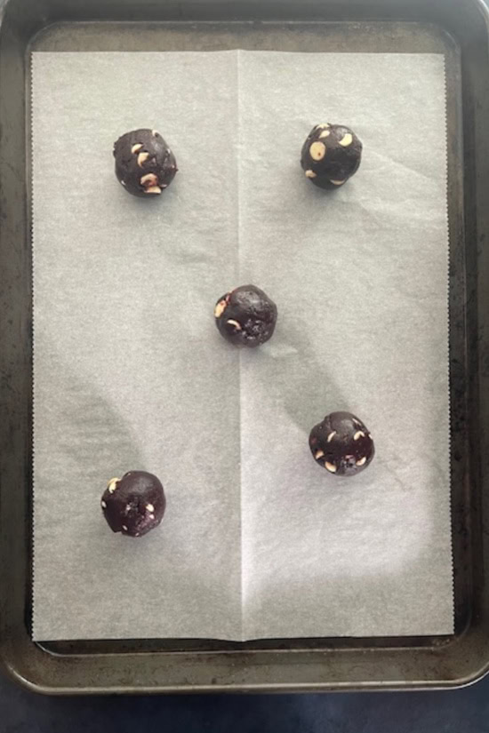 A parchment lined baking sheet with five cookie dough balls on it.