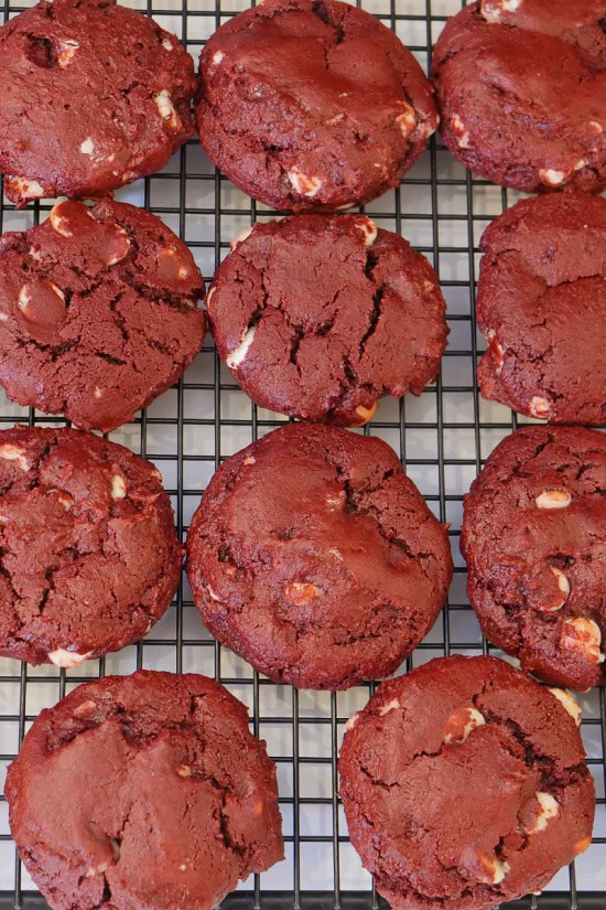 A wire cooling rack with eleven baked red velvet cookies on it.