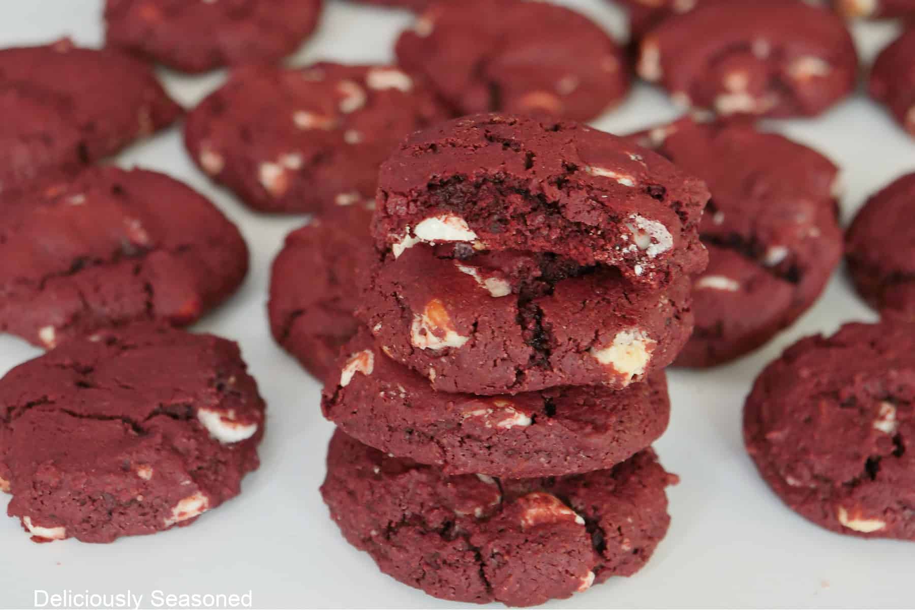 A white surface with two dozen red velvet cookies on it.