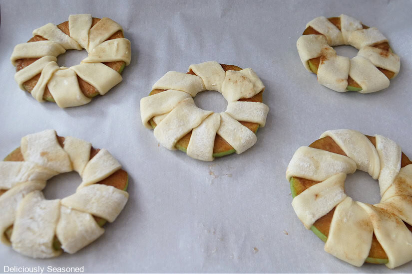 Apple rings wrapped with pastry strips on a baking sheet.