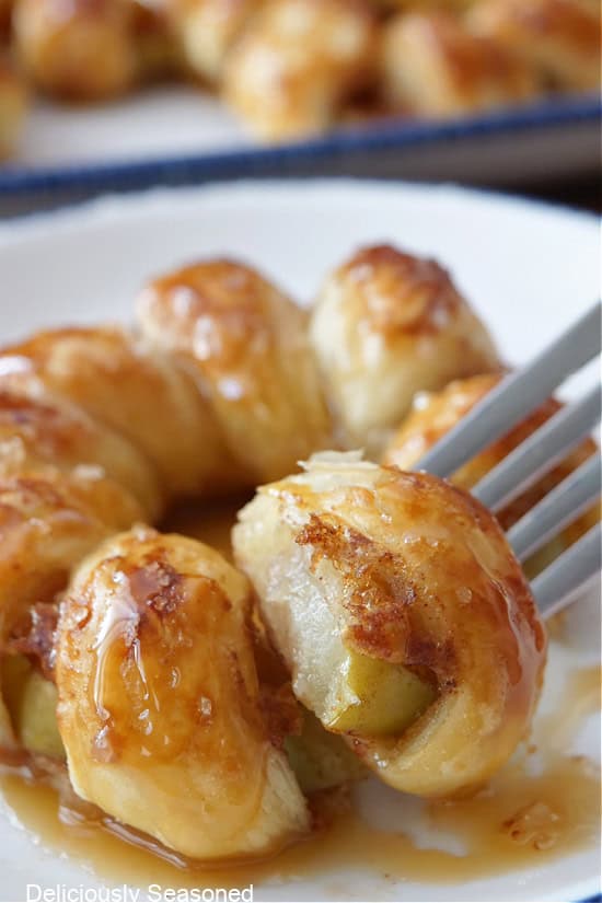 A white plate with a apple pastry ring on it with a bite on a fork.