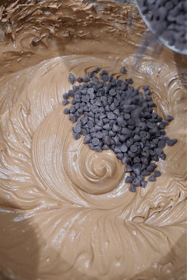 A silver bowl with the chocolate cream pie mixture in it with mini chocolate chips being poured into the batter.